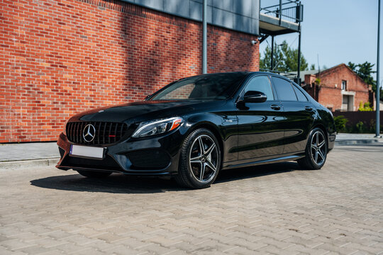 Photo of a black Mercedes C-Class W205 AMG C43. They show details of the car from the outside. Rims, emblems, headlights, lamps in a sporty style. The model stands in a loft style.