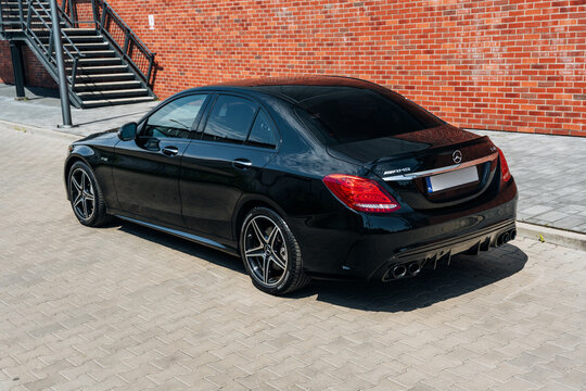 Photo of a black Mercedes C-Class W205 AMG C43. They show details of the car from the outside. Rims, emblems, headlights, lamps in a sporty style. The model stands in a loft style.