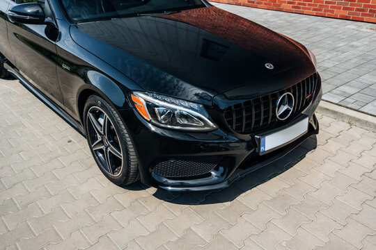 Photo of a black Mercedes C-Class W205 AMG C43. They show details of the car from the outside. Rims, emblems, headlights, lamps in a sporty style. The model stands in a loft style.