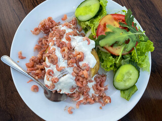 Baked potato with sour cream, North Sea crabs and salad with fresh vegetables on a plate directly above view
