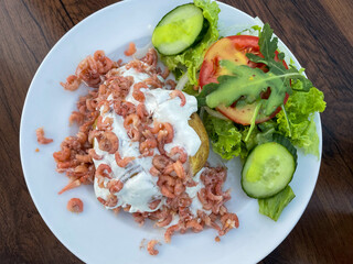 Baked potato with sour cream, North Sea crabs and salad with fresh vegetables on a plate directly above view