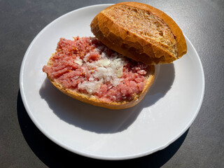 Traditional german snack Mett wheat bun with raw minced pork with onion, salt and spices on a plate directly above view