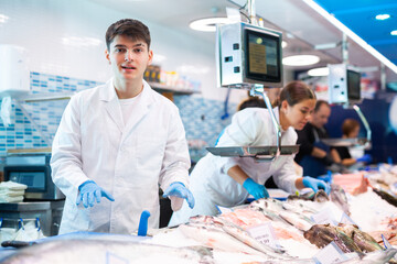 Smiling young shop assistants staying behind counter in fish shop with big assortment