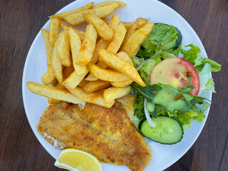 Roasted plaice fillet fish with french fries and green salad with cucumber and tomato on a plate...