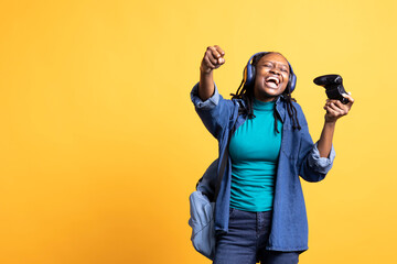 Euphoric african american teenager playing intense gaming console game, celebrating win, studio...