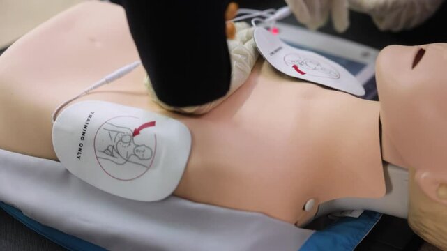 close up CPR training using and an AED and bag mask valve on an adult training manikin. Two men train using an automated external defibrillator AED on a dummy.