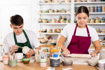 Fototapeta premium Young man and young woman making pottery from clay in workshop