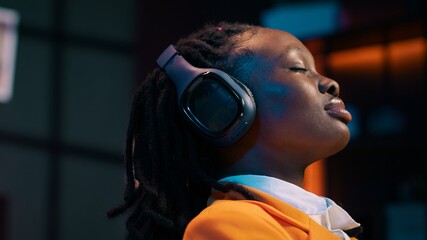 Carefree student finishes creating a presentation and relaxes with music on audio headset, resting after long researching session. African american girl chilling with ambience tunes. Camera A.