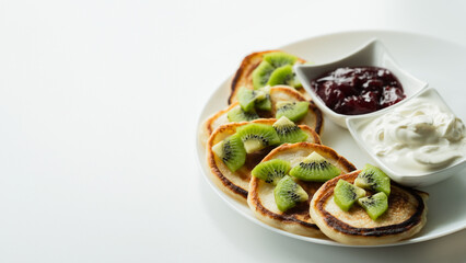 Plate of pancakes dripping with cherry jam, sour cream and kiwi pieces with white background.. Copy space for text. Mockup for menu, Pancake day
