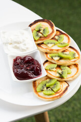 Plate of pancakes dripping with cherry jam, sour cream and kiwi pieces with white background.. Copy space for text. Mockup for menu, Pancake day