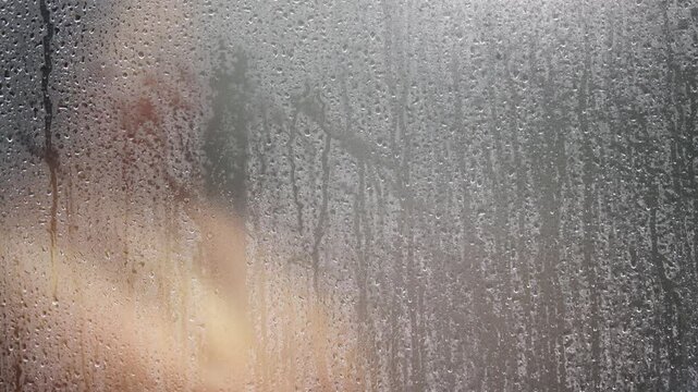 Woman showering in the shower room close up with a water drop on glass door