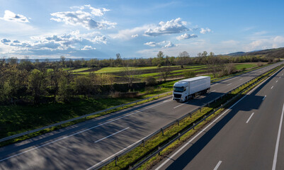 White Trucks with containers on highway. Large Transportation Truck on a highway road through the countryside with blue sky and white clouds background. © Bojan
