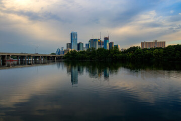 Naklejka premium Austin Texas stunning skyline from the boardwalk at Lady Bird Lake. Sleek skyscrapers reflect in the calm waters, doubling the cityscape's beauty.