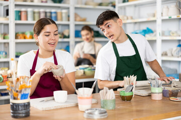 Fototapeta premium Young woman and young man sculpting ceramic product in workshop