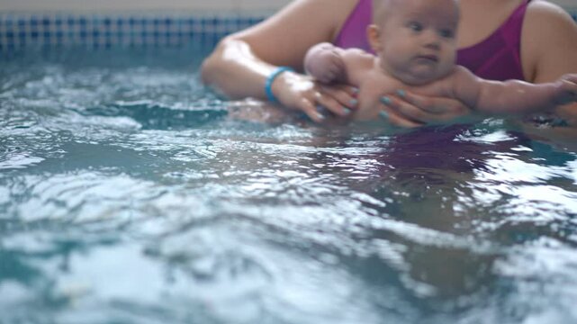 Close-up. An unrecognizable woman accustoms an baby to water by bathing him in a swimming pool for babies with optimal water temperature