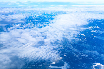 Scenic sky view from airplane, featuring fluffy clouds. sky is blue with clouds and mountains in the background. The clouds are fluffy and white, and the mountains are covered in snow