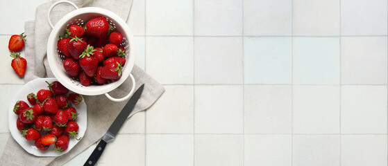 Colander and plate with fresh sweet strawberries on white tile background