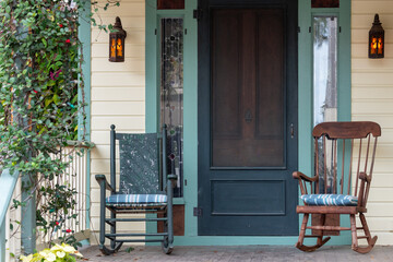 Two antique wooden rocking chairs on the front porch of a country style house. The door is wooden...