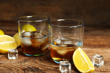 Glasses of rum with ice cubes and lime on wooden background