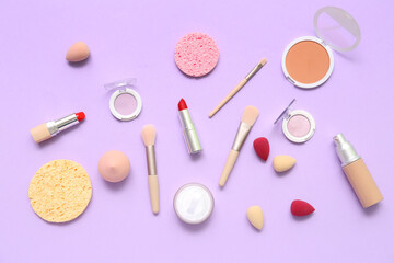 Decorative cosmetics with makeup brushes and sponges on lilac background