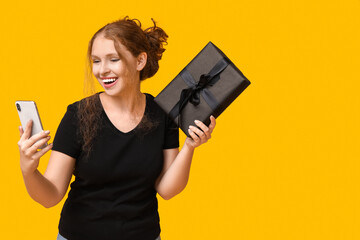 Beautiful young woman with mobile phone and gift box on yellow background. Black Friday sale