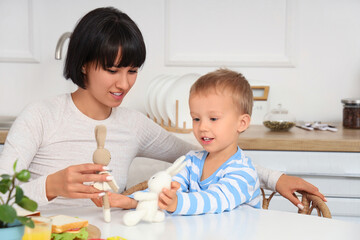 Fototapeta premium Young mother and her little son playing with toys at table in kitchen