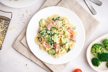 Plate of tasty pasta with broccoli, tomatoes and napkin on white background