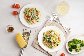 Plates of tasty pasta with broccoli, tomatoes and cutlery on white background
