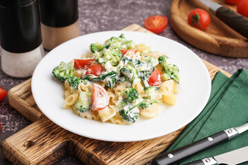 Plate of tasty pasta with broccoli and tomatoes on grunge grey background