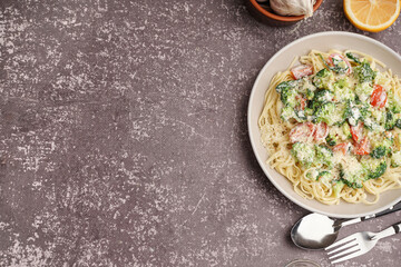 Plate of tasty pasta with broccoli, cheese and tomatoes on grunge grey background