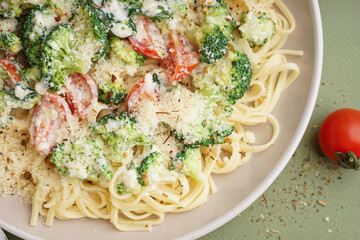 Plate of tasty pasta with broccoli, cheese and tomatoes on green background