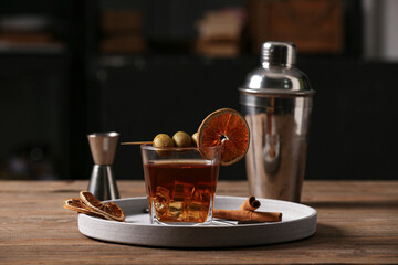 Tray with glass of Old Fashioned Cocktail, cinnamon sticks, olives and dried orange slices on wooden table