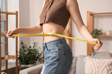 Young woman measuring her waist at home. Weight loss concept