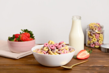Bowls with colorful sweet cereal rings, strawberries and bottle of milk on wooden table