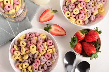 Bowls with colorful sweet cereal rings and strawberries on white table