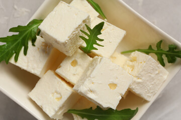 Bowl with cubes of feta cheese and arugula on grey background, closeup