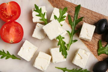 Board with cubes of feta cheese, arugula, cherry tomato and olives on white background, closeup