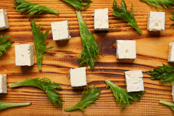 Cubes of feta cheese and lettuce on wooden background, closeup