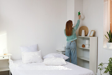 Young woman removing mold from wall in bedroom, back view