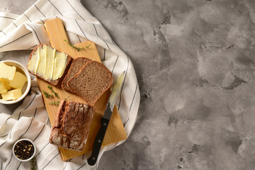 Wooden board with bread slices and bowl of fresh butter on grey background