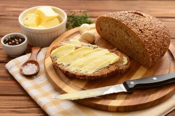 Board with fresh bread, different spices and bowl of butter on wooden background