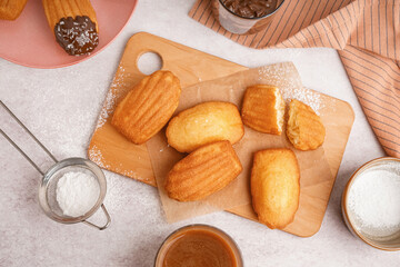 Wooden board with baking paper and delicious madeleines on white background