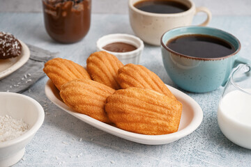 Plate with delicious madeleines, coconut flakes and cup of coffee on white grunge background