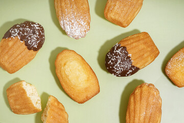 Delicious madeleines with chocolate, powdered sugar and coconut flakes on green background