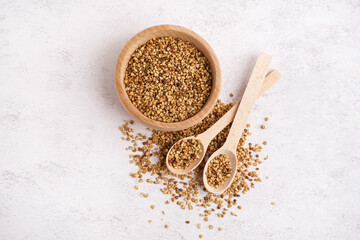 Wooden bowl and spoons with raw buckwheat grains on light background