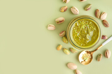 Tasty pistachio paste in jar and spoon on green background