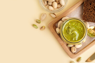 Wooden tray with jar of pistachio paste on beige background