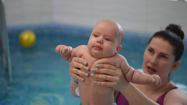A female trainer pulls a baby out of the pool, where it had been receiving water treatments and hands it to an unrecognizable woman, who wraps it in a large red towel