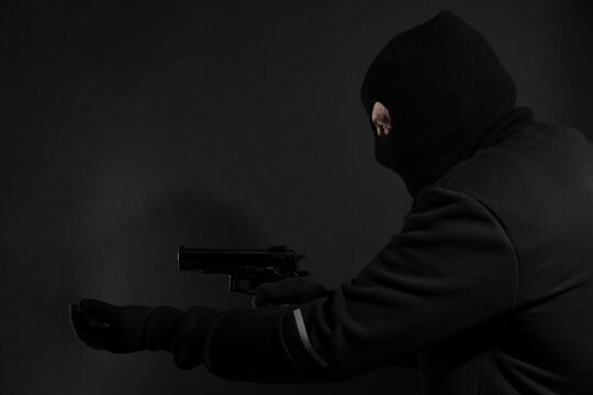 Dangerous masked criminal with gun on black background. Armed robbery