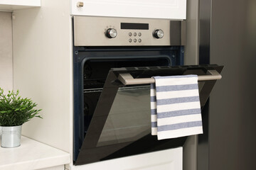 Open electric oven with striped towel in kitchen. Cooking appliance